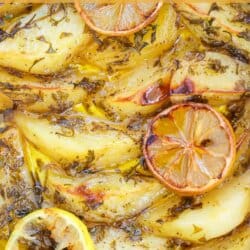Potato wedges covered in a zesty lemon sauce with herbs in a white casserole dish.