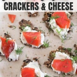 Crackers with cream cheese and pieces of salmon garnished with fresh dill on a cream plate.