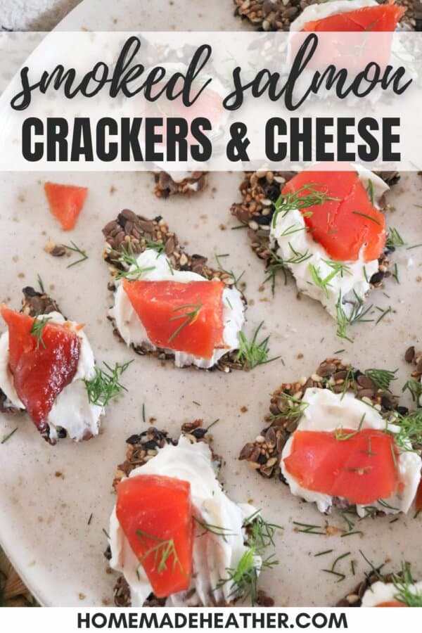 Crackers with cream cheese and pieces of salmon garnished with fresh dill on a cream plate.