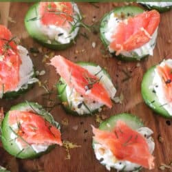 Small rounds of cucumber slices topped with cream cheese, smoked salmon and garnished with fresh dill and lemon zest on a wooden cutting board.