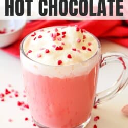 Red velvet hot chocolate in a clear mug topped with whipped cream and sprinkles.
