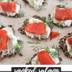 Crackers with cream cheese and pieces of salmon garnished with fresh dill on a cream plate.