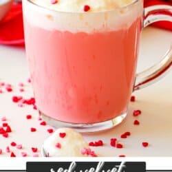 Red velvet hot chocolate in a clear mug topped with whipped cream and sprinkles.
