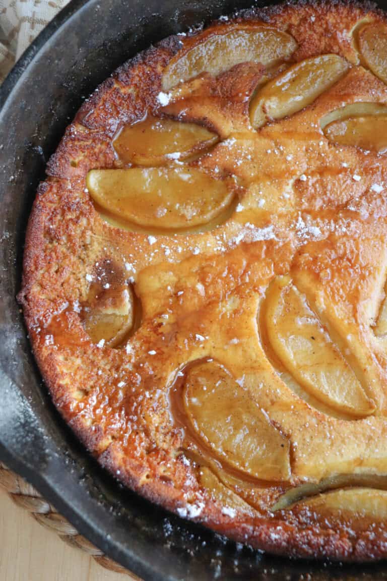 Dutch baby with apple slices and a caramel drizzle in a cast iron skillet.