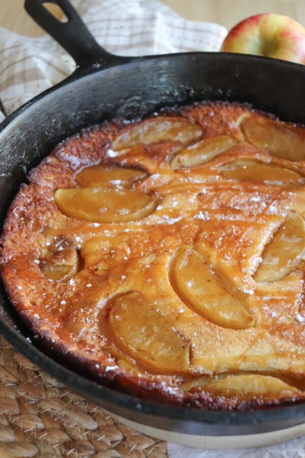 Dutch baby with apple slices and a caramel drizzle in a cast iron skillet.