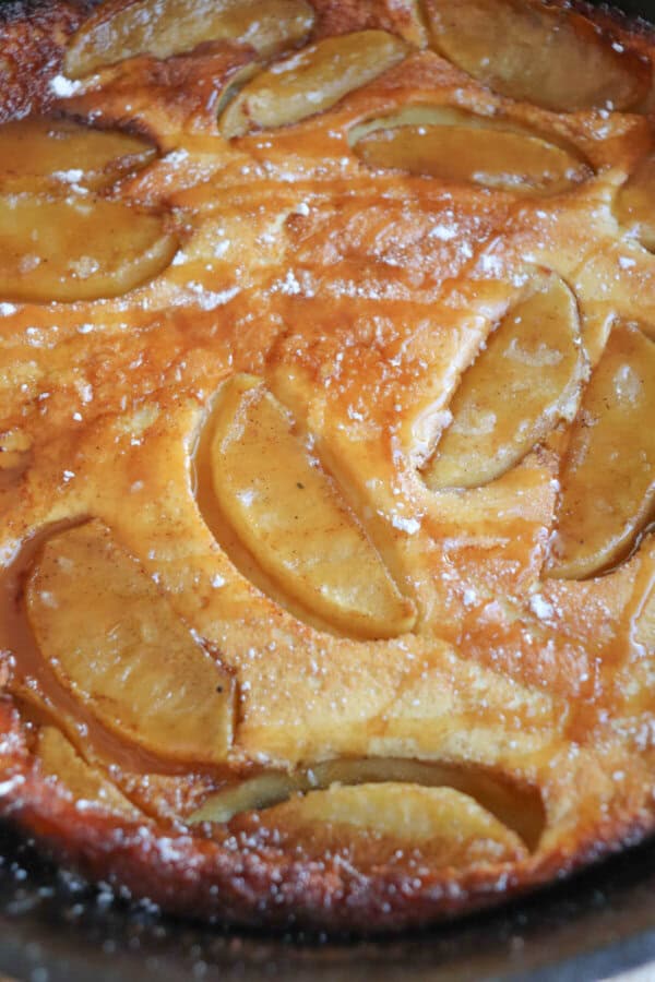 Dutch baby with apple slices and a caramel drizzle in a cast iron skillet.