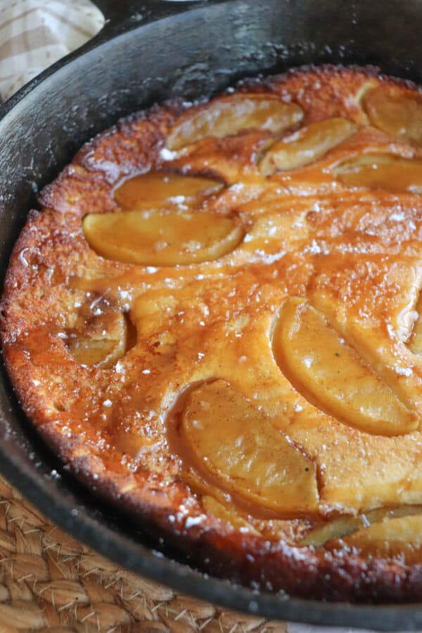 Dutch baby with apple slices and a caramel drizzle in a cast iron skillet.