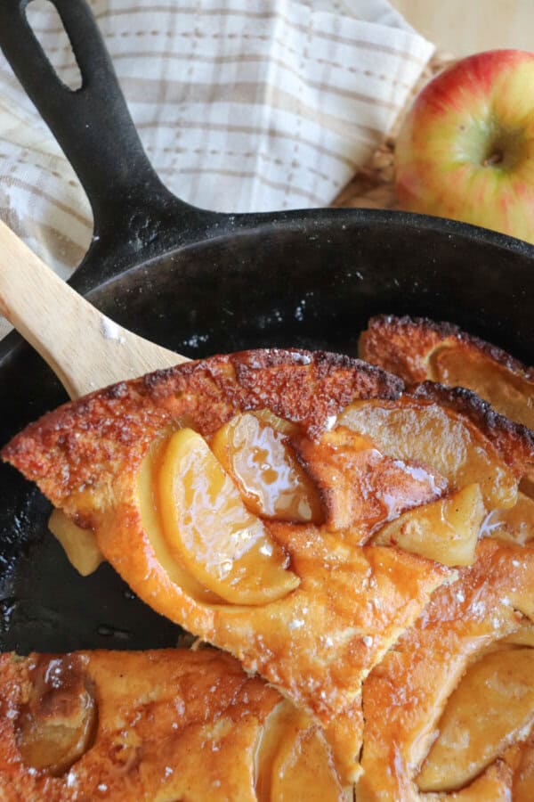 Dutch baby with apple slices and a caramel drizzle in a cast iron skillet.