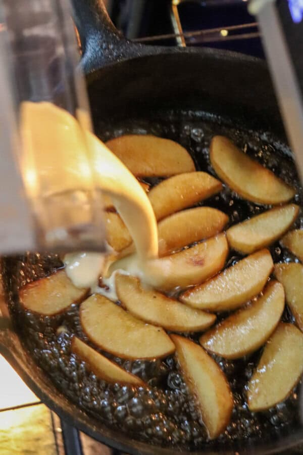 Dutch baby batter being poured into a skillet full of cooked apples.