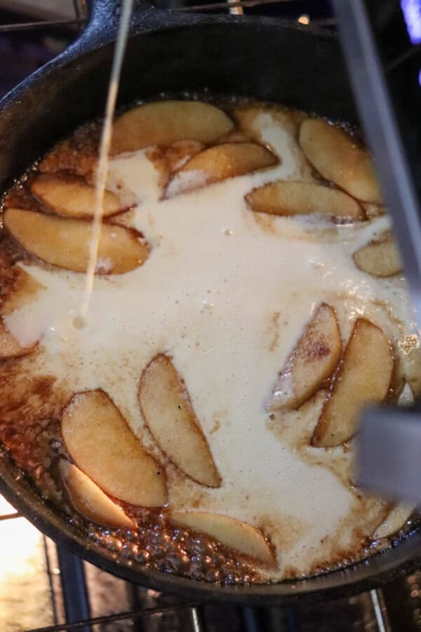 Apple slices with pancake batter in a cast iron skillet.