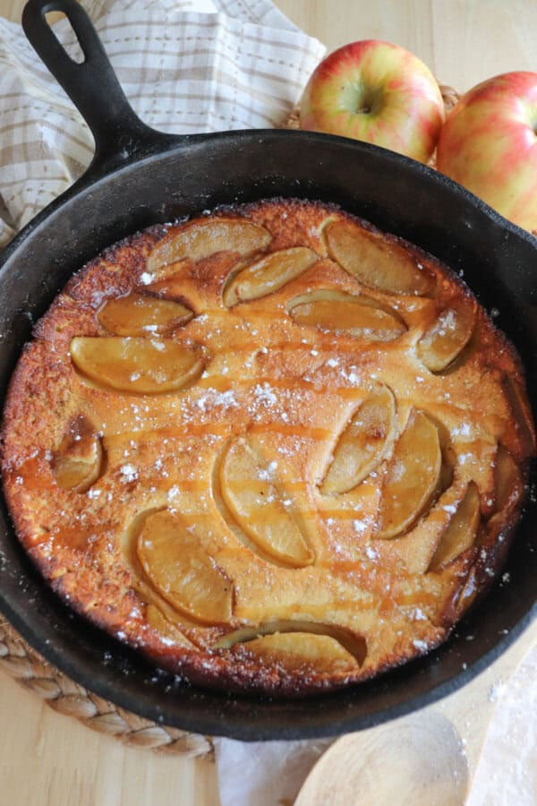 Dutch baby with apple slices and a caramel drizzle in a cast iron skillet.