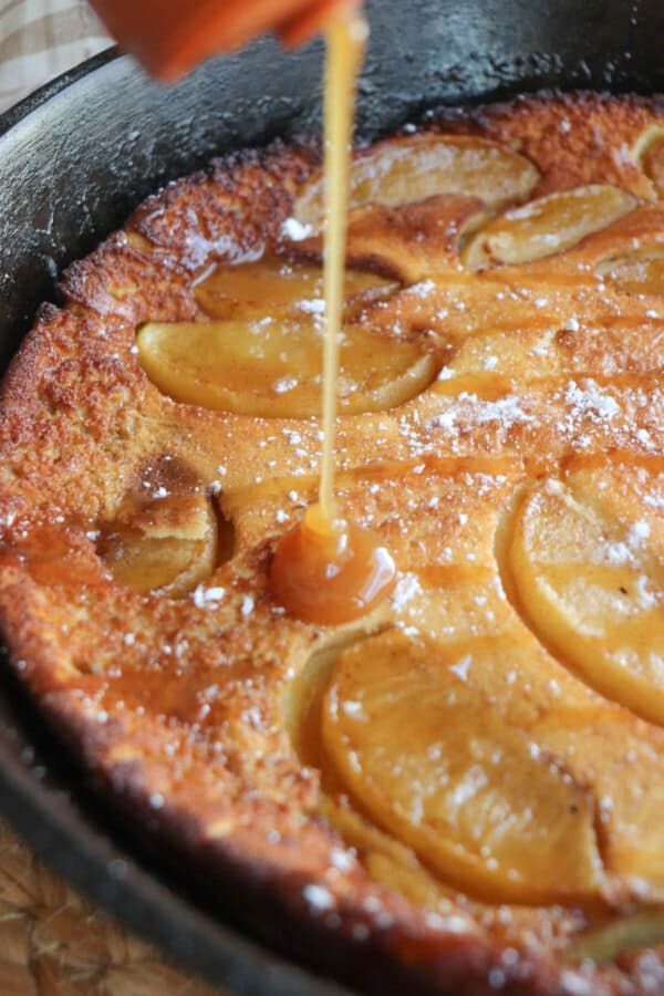 Caramel being drizzled onto an apple dutch baby in a cast iron skillet.