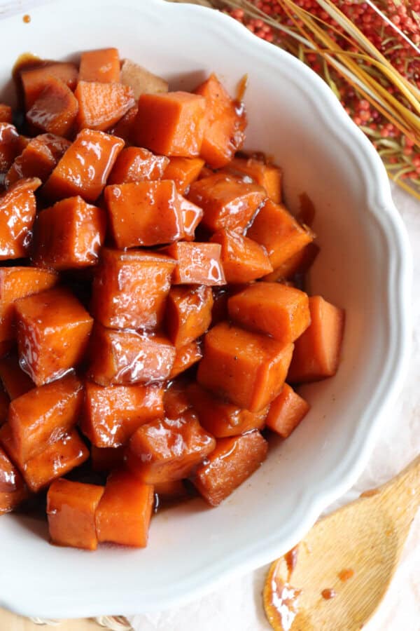 Sweet potatoes covered in a brown sugar glaze in a large white bowl.