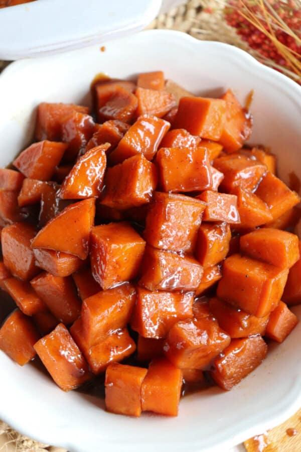 Sweet potatoes covered in a brown sugar glaze in a large white bowl.