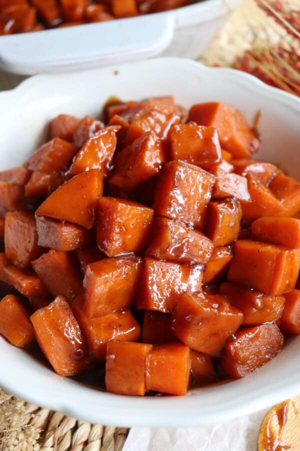 Sweet potatoes covered in a brown sugar glaze in a large white bowl.