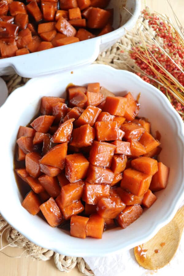 Sweet potatoes covered in a brown sugar glaze in a large white bowl.