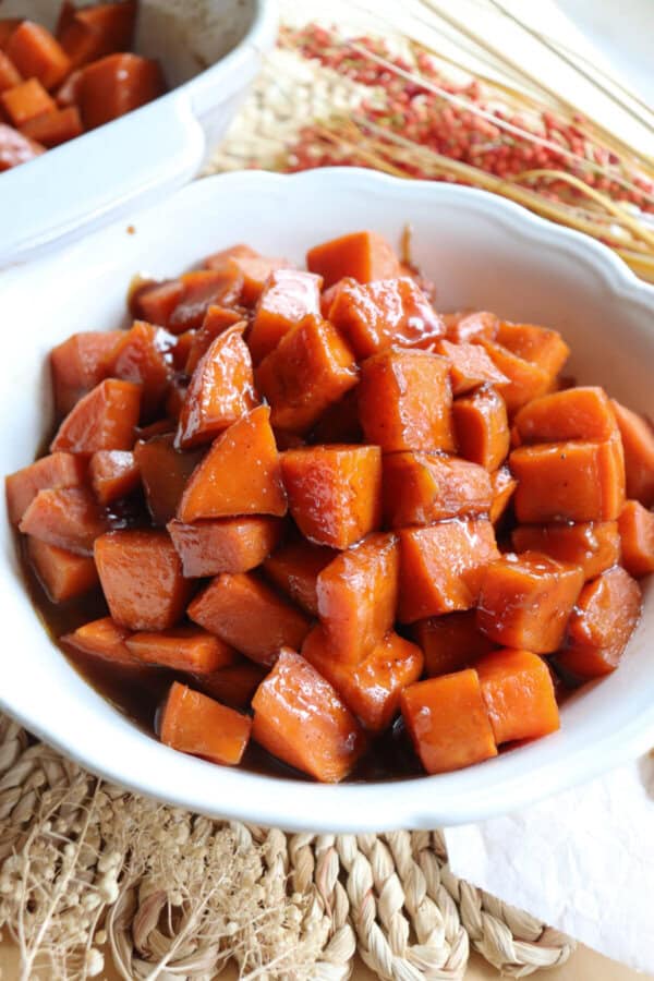 Sweet potatoes covered in a brown sugar glaze in a large white bowl.