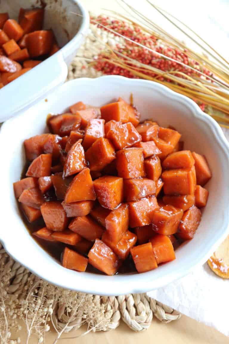 Sweet potatoes covered in a brown sugar glaze in a large white bowl.