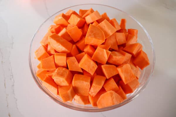 Sweet potatoes peeled and cut into cubes in a clear glass bowl on a white ocunter.