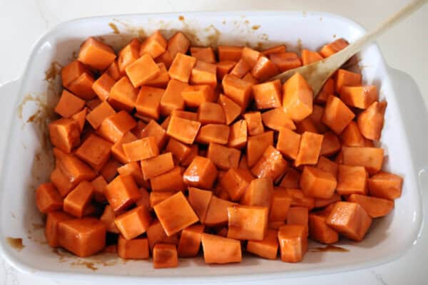 Cubed sweet potatoes mixed with a brown sugar glaze in a large white casserole dish.