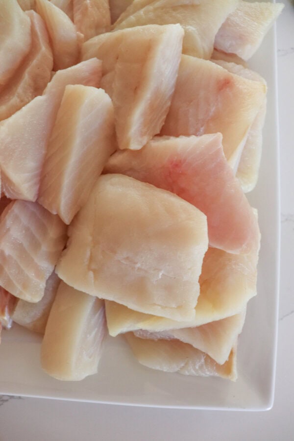 White fish fillets cut into squares and stacked on a white plate.