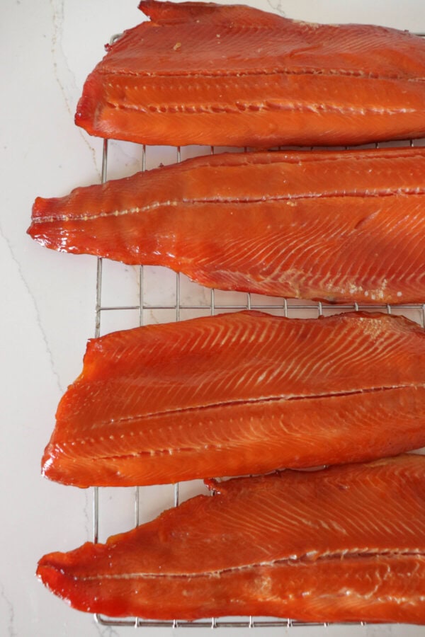 The ends of four cold smoked salmon fillets on a wire rack on a white counter.