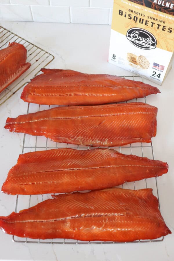 Four cold smoked salmon fillets on a wire rack on a white counter with a box of Bradley Smoker wood pucks in the background.