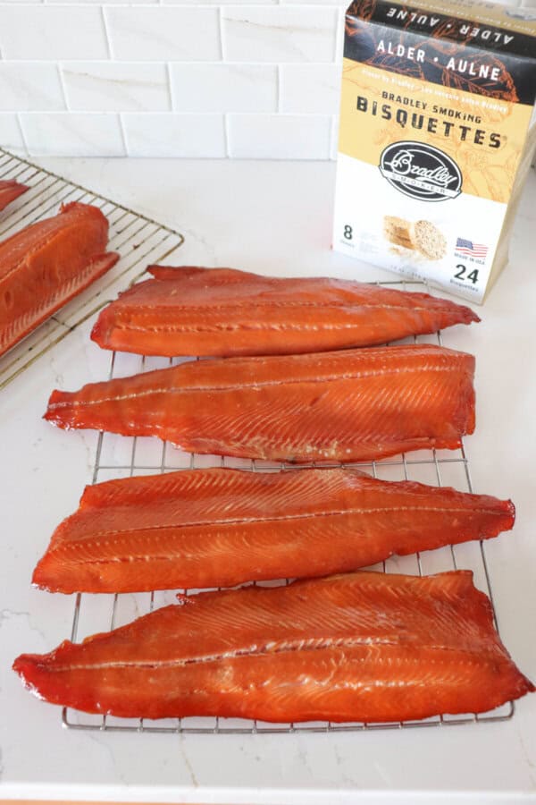 Four cold smoked salmon fillets on a wire rack on a white counter with a box of Bradley Smoker wood pucks in the background.