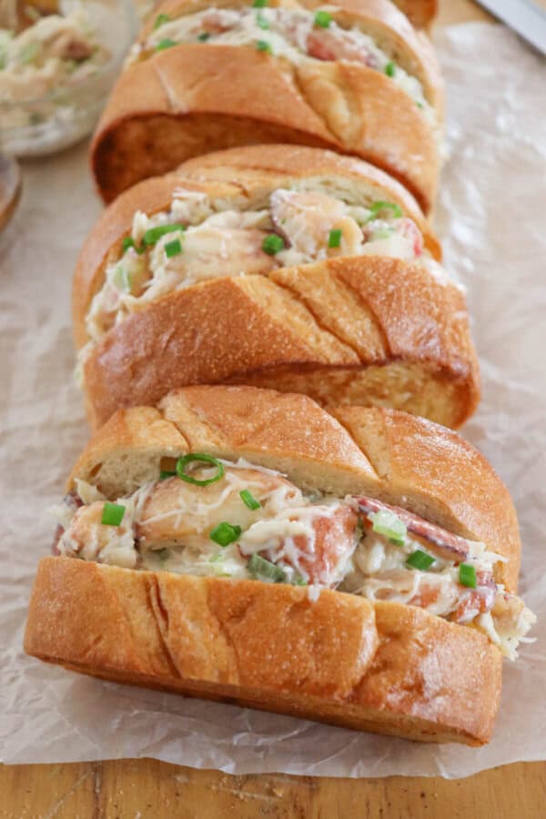 Crab salad with green onions and mayonnaise sandwiched between to slices of grilled garlic bread on a parchment paper lined surface.