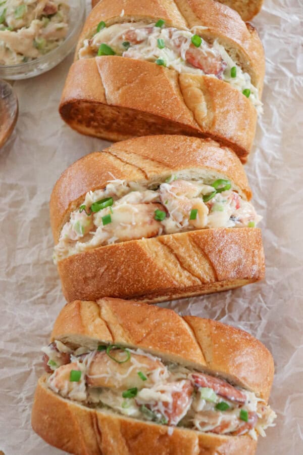 Crab salad with green onions and mayonnaise sandwiched between to slices of grilled garlic bread on a parchment paper lined surface.