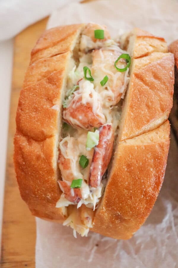 Crab salad with green onions and mayonnaise sandwiched between to slices of grilled garlic bread on a parchment paper lined surface.