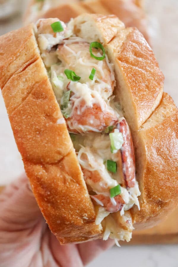 Crab salad with green onions and mayonnaise sandwiched between to slices of grilled garlic bread held in a hand.