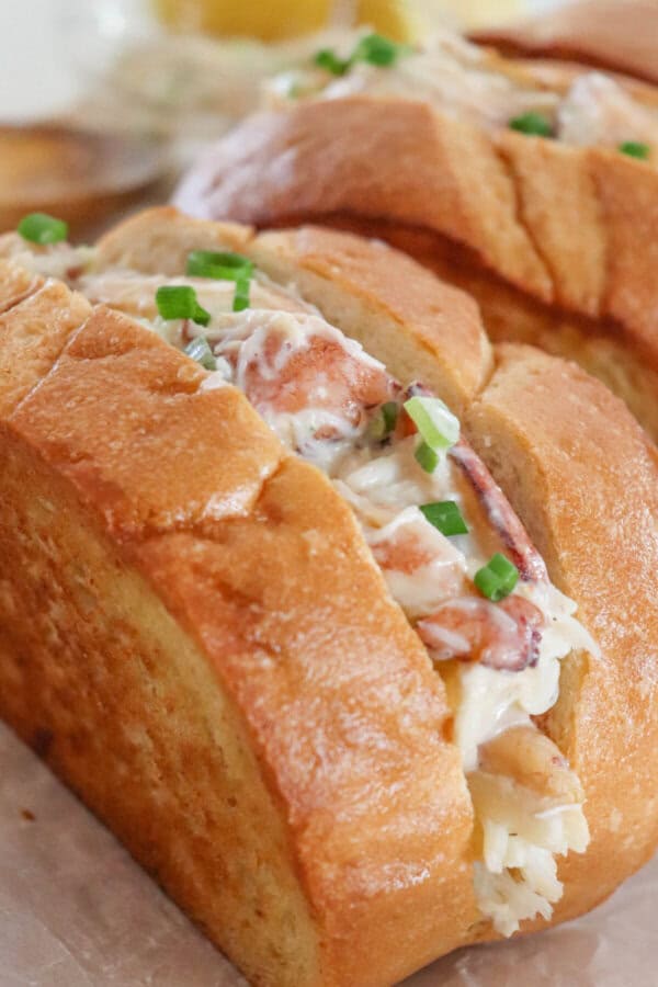 Crab salad with green onions and mayonnaise sandwiched between to slices of grilled garlic bread on a parchment paper lined surface.