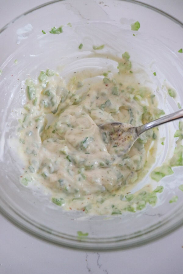 Mayonnaise, vegetables and spices mixed in a clear glass bowl.