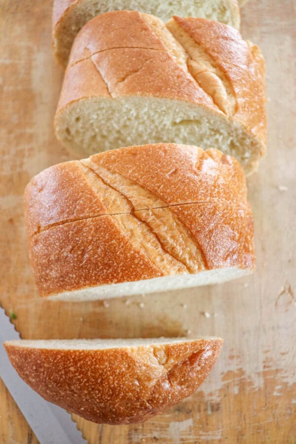 French loaf cut into slices on a wooden cutting board.