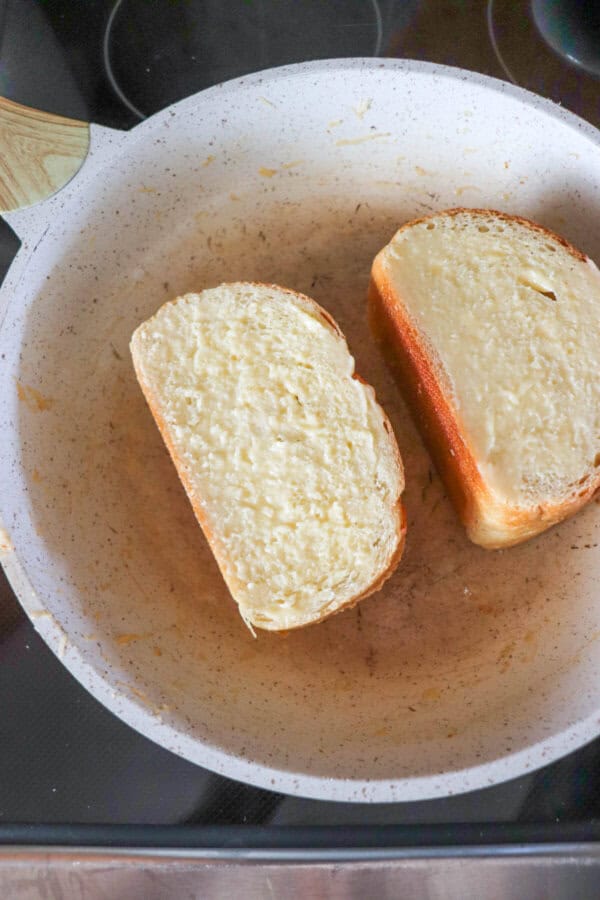 Slices of french bread with garlic butter on them in a white skillet on a stove top.