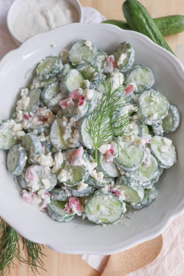 Sliced cucumbers in tzatziki with diced pickled onions and dill in a white bowl.