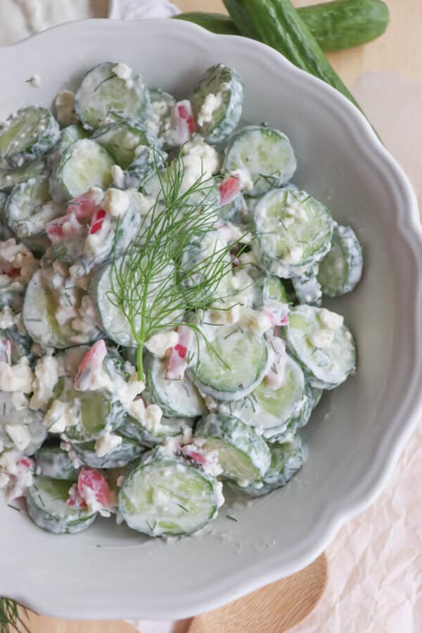 Sliced cucumbers in tzatziki with diced pickled onions and dill in a white bowl.