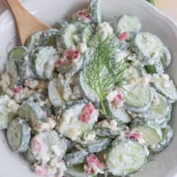 Sliced cucumbers in tzatziki with diced pickled onions and dill in a white bowl.