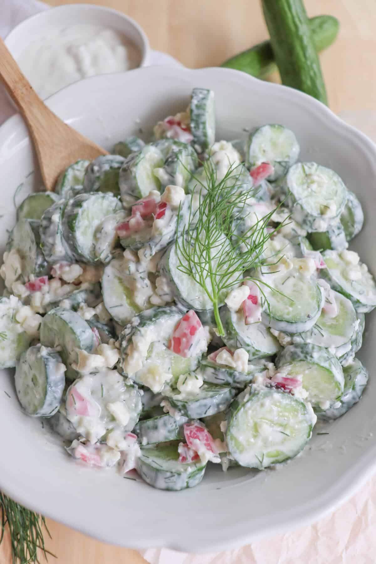 Sliced cucumbers in tzatziki with diced pickled onions and dill in a white bowl.