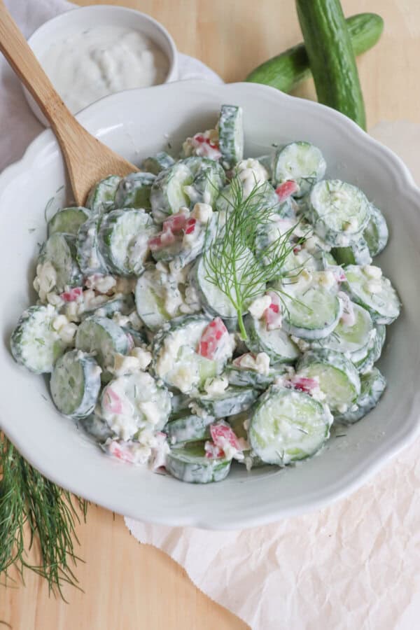Sliced cucumbers in tzatziki with diced pickled onions and dill in a white bowl.