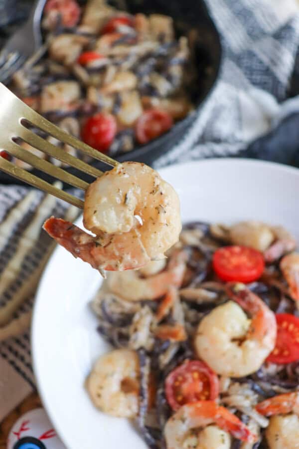 Purple and white linguine noodles in a cream sauce topped with shrimp and cherry tomatoes with a shrimp on a gold fork.