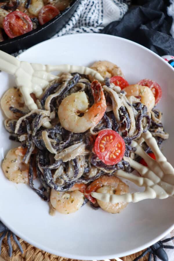 Purple and white linguine noodles in a cream sauce topped with shrimp and cherry tomatoes with skeleton hands in a white bowl.