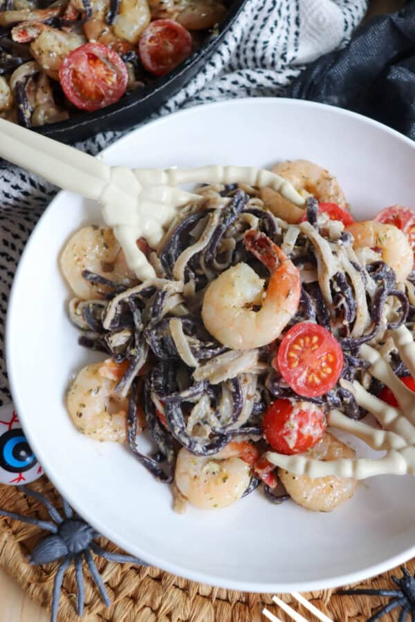 Purple and white linguine noodles in a cream sauce topped with shrimp and cherry tomatoes with skeleton hands in a white bowl.