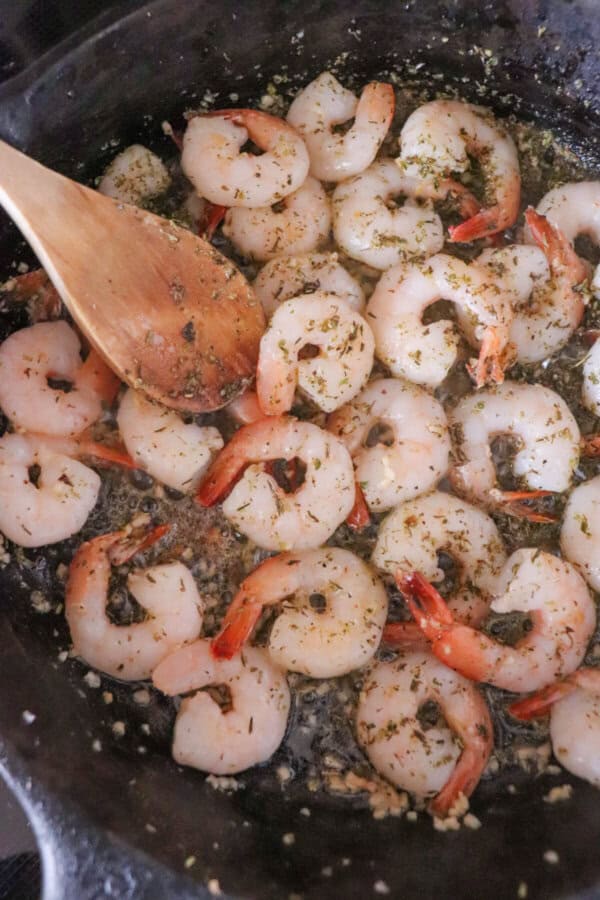 Shrimp being sauteed in a cast iron skillet with a wooden spoon.