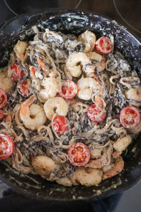Purple and white linguine noodles in a cream sauce topped with shrimp and cherry tomatoes.