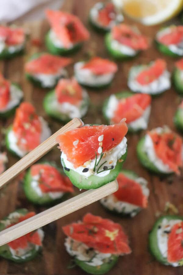 Small rounds of cucumber slices topped with cream cheese, smoked salmon and garnished with fresh dill and lemon zest on a wooden cutting board.