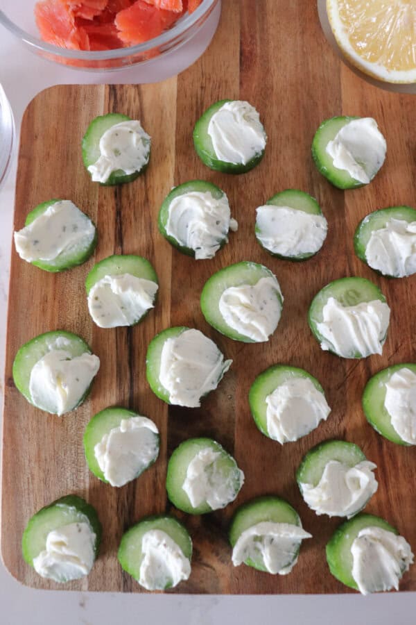 Small rounds of cucumber slices topped with cream cheese on a wooden cutting board.