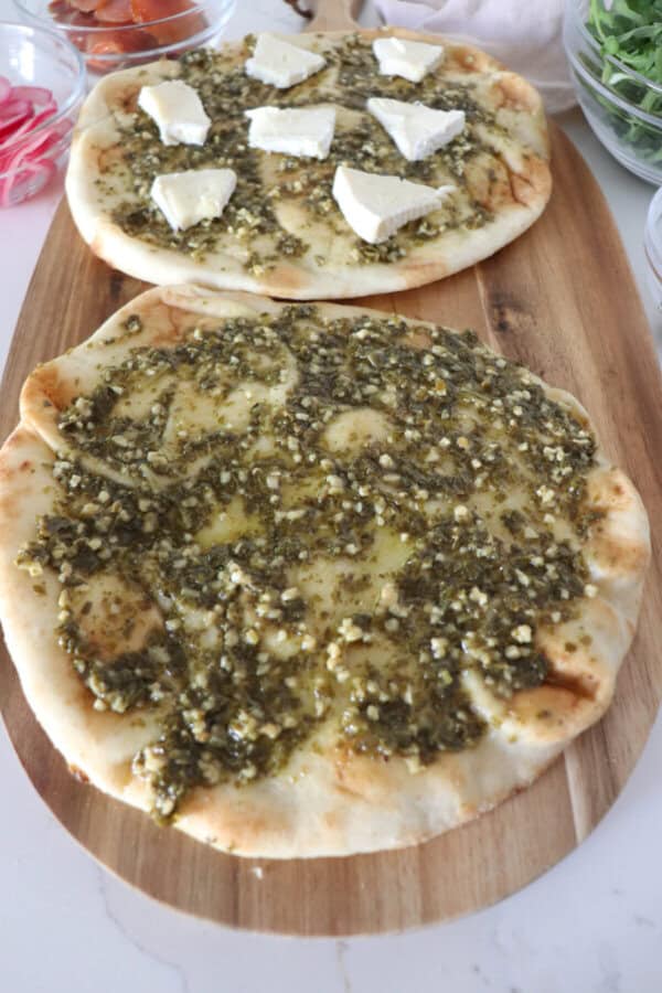 Naan bread covered in pesto sauce on a wooden cutting board.