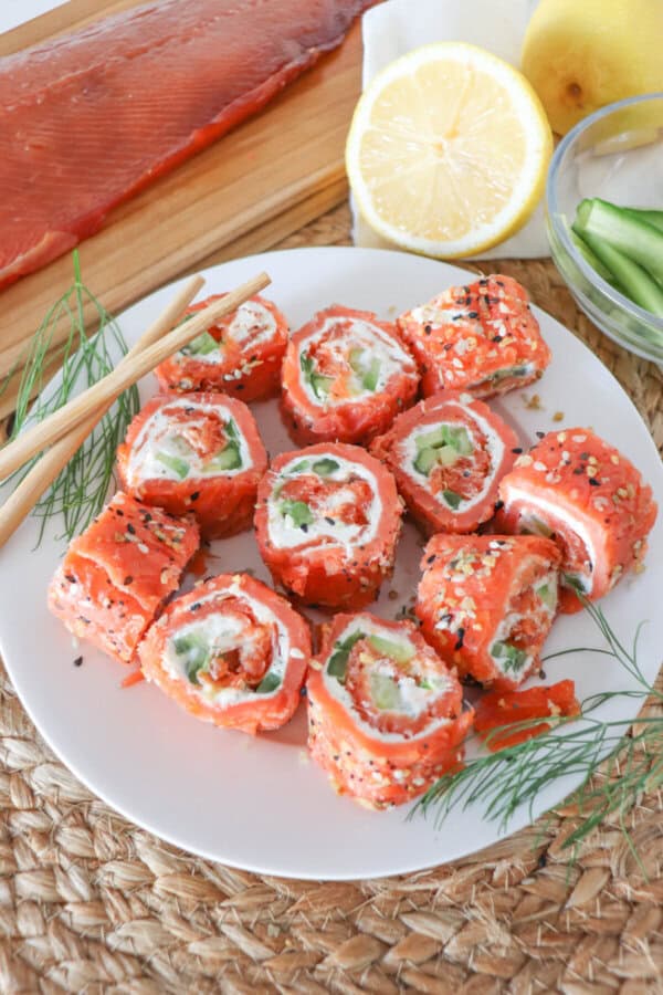 Smoked salmon rolled around cream cheese, cucumbers and avocado and cut into sushi style rolls on a white plate.